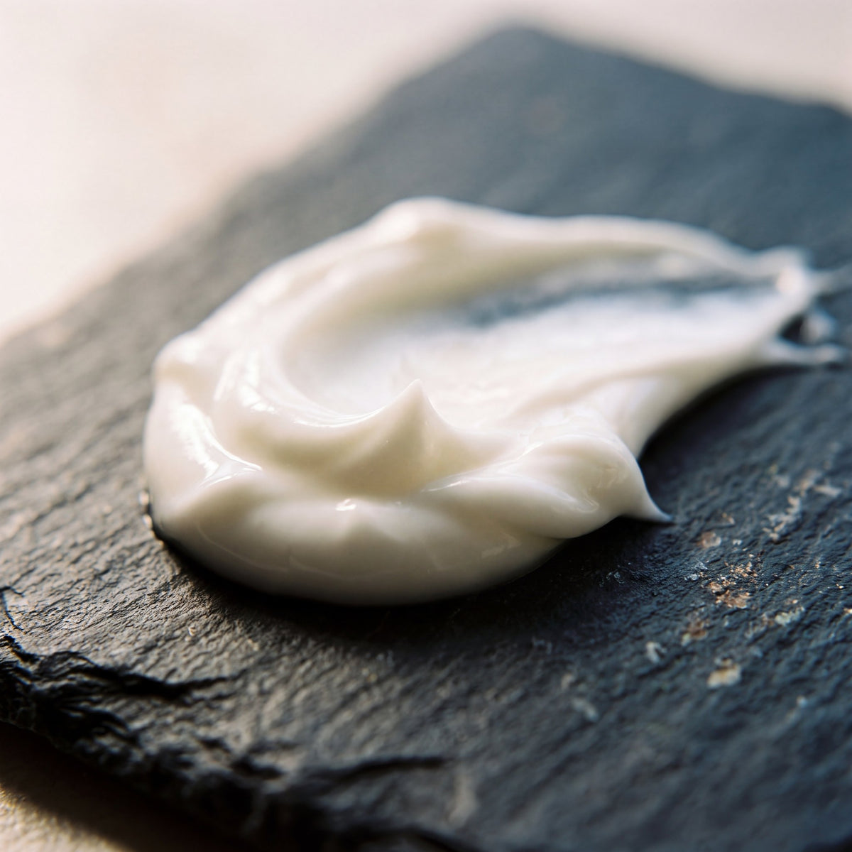 Swirl of creamy white Night Magnesium Lotion on a dark slate surface